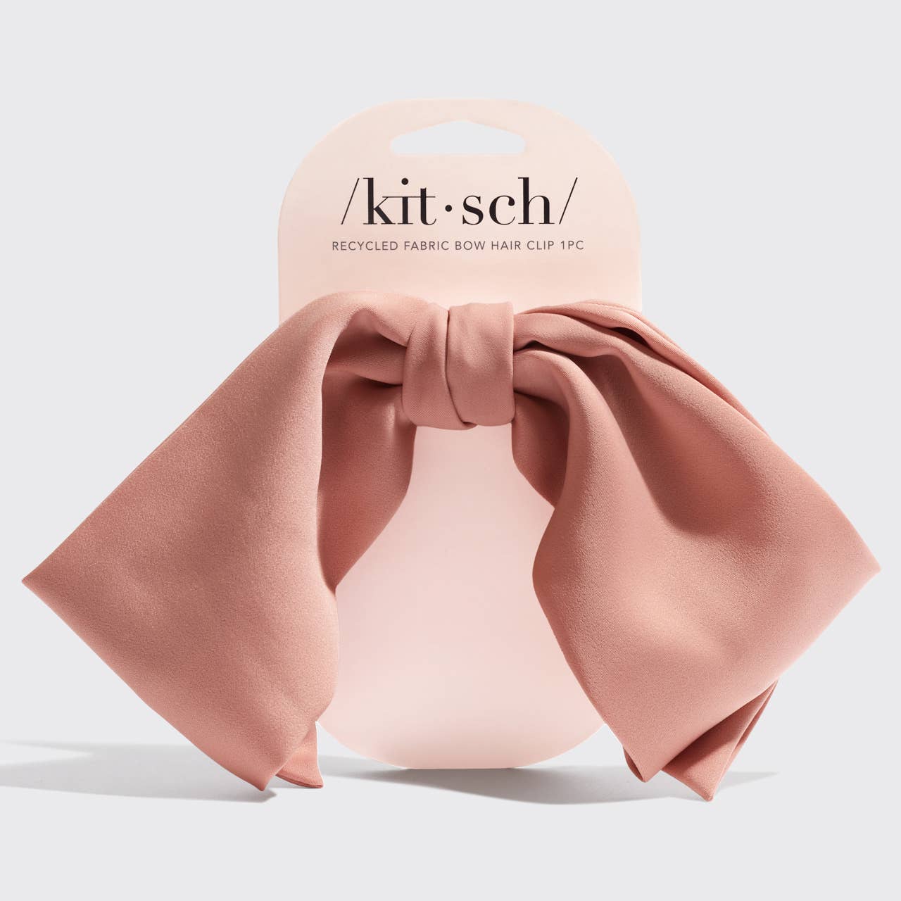 Pink bow hair clip with 'kit-sch' packaging on a light gray background