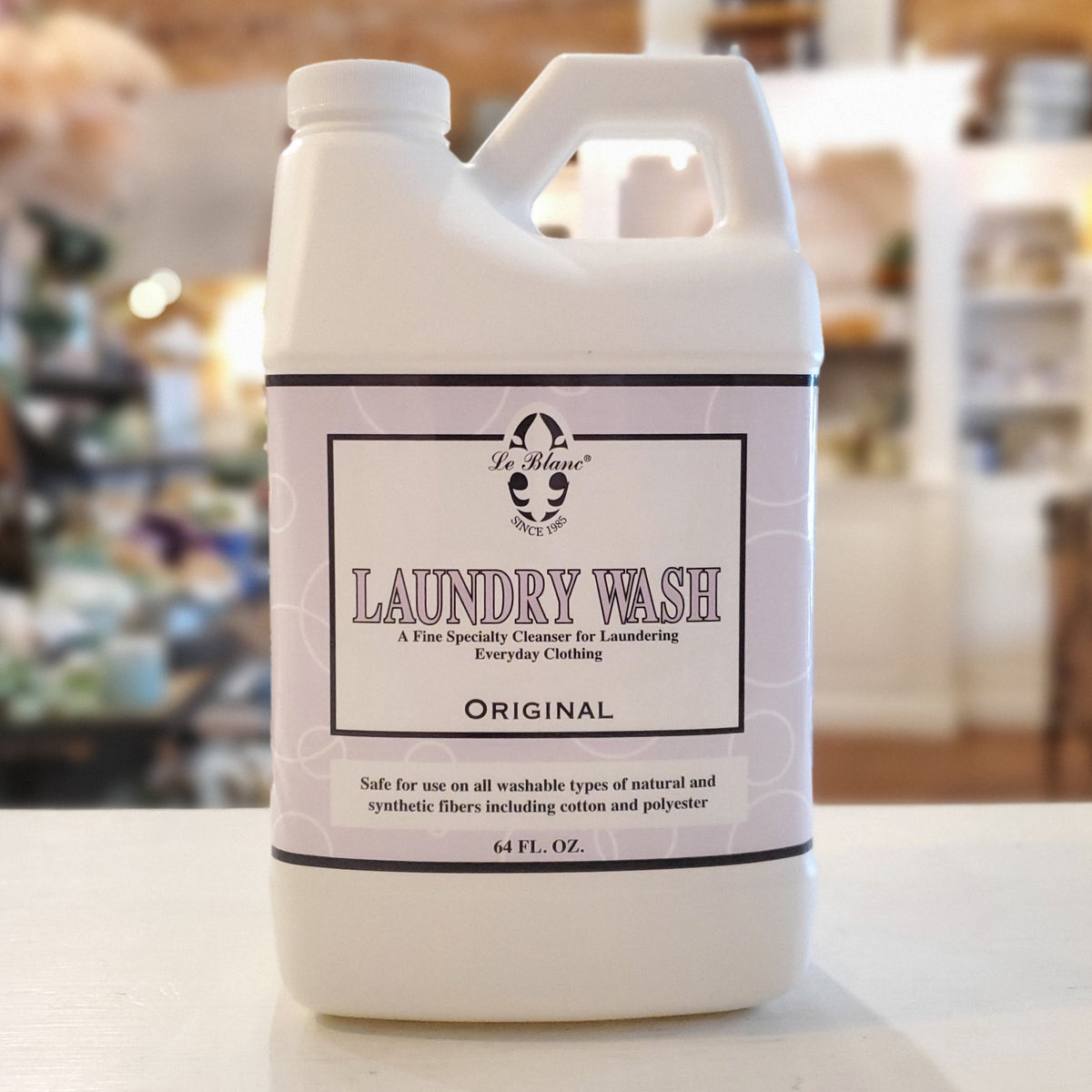 A white plastic bottle of Le Blanc laundry detergent with a label that reads 'LAUNDRY WASH Original'. The bottle is placed on a counter with a blurred background.